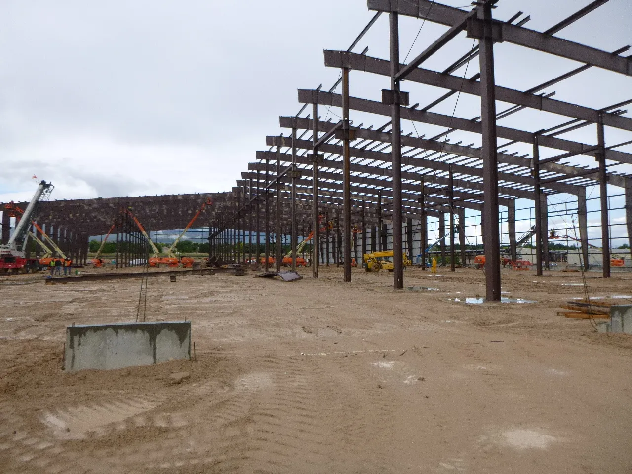 DSSJ steel rigid frames rising beyond a concrete pier, with boom lifts and a crane